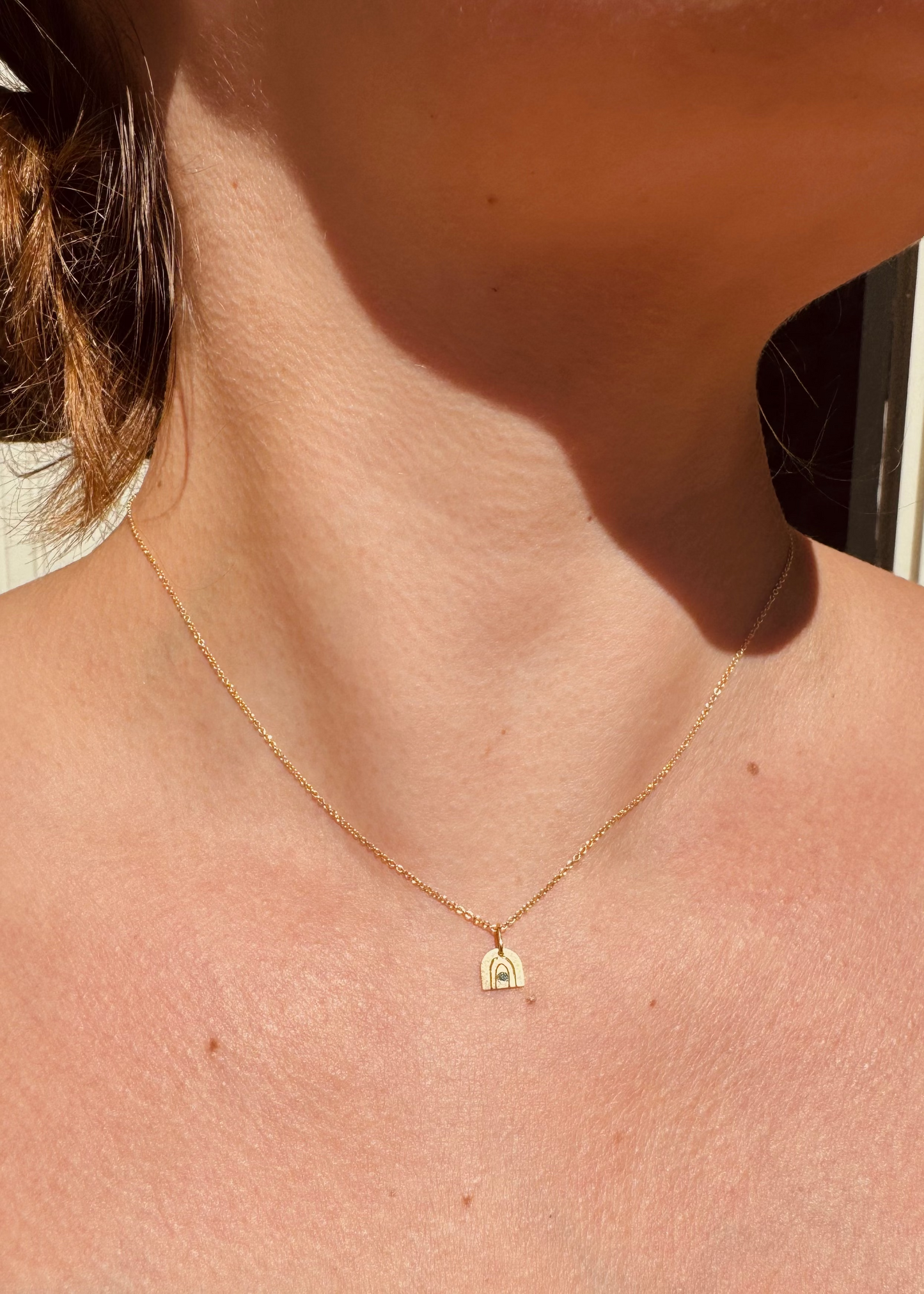 Person wearing Julez Bryant fine jewelry 14k yellow gold teal diamond Teeny Tiny Joy Rainbow Charm Necklace