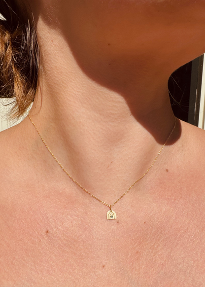 Person wearing Julez Bryant fine jewelry 14k yellow gold teal diamond Teeny Tiny Joy Rainbow Charm Necklace