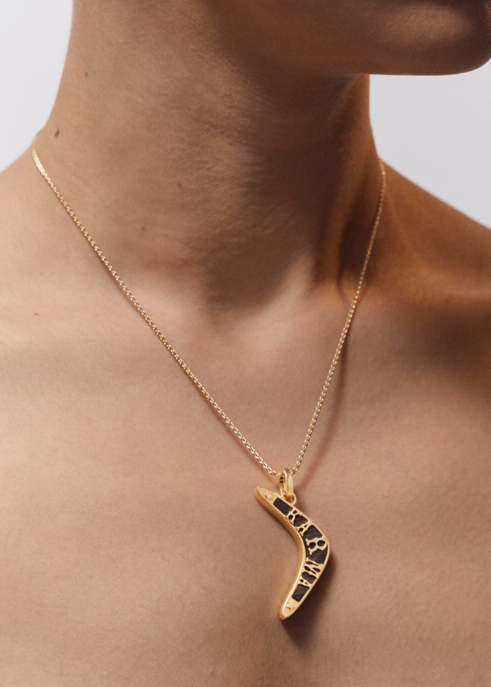 Person wearing Marie Lichtenberg fine jewelry 18k yellow gold Karma Boomerang Pendant with Ebony Necklace