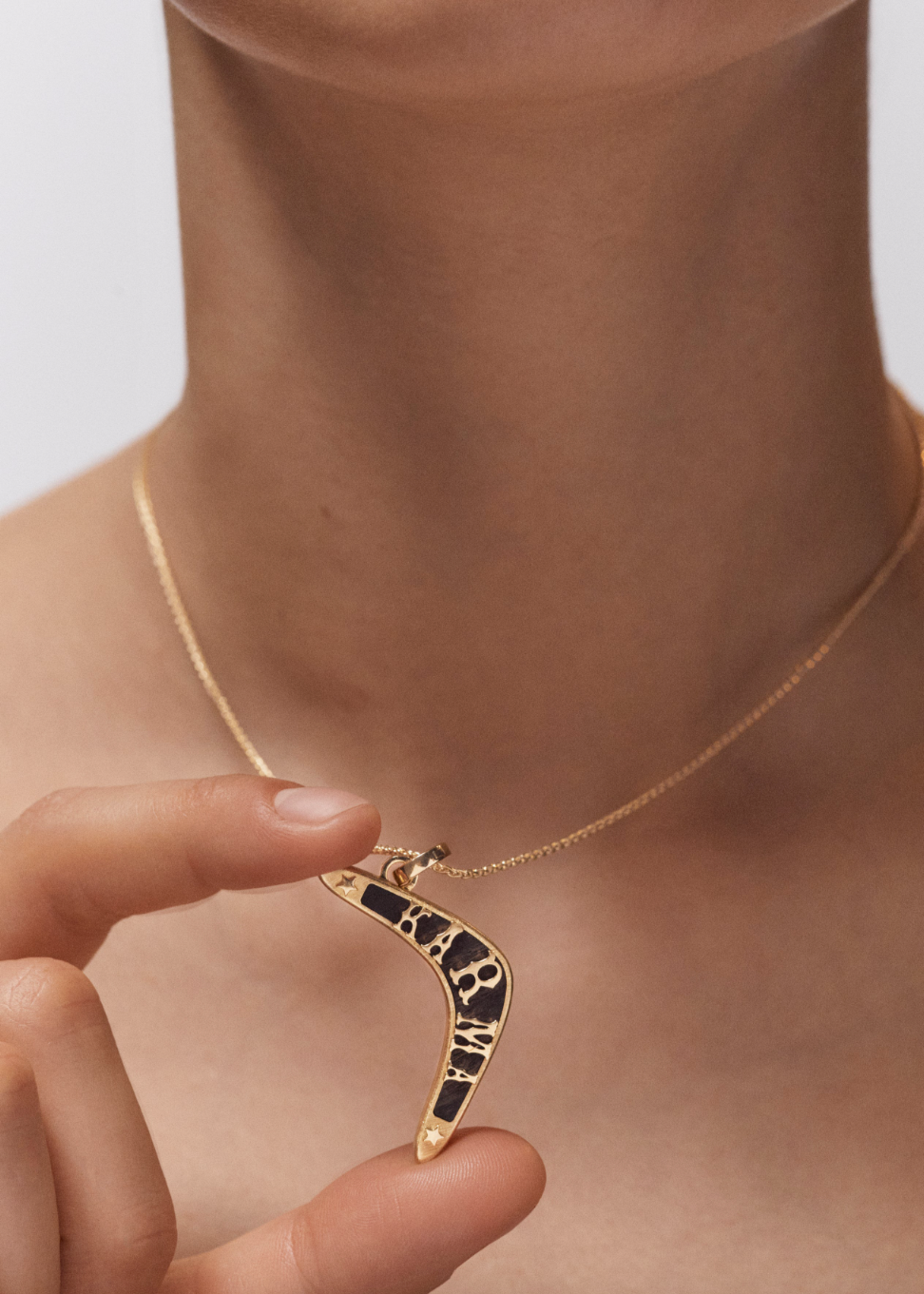 Person wearing Marie Lichtenberg fine jewelry 18k yellow gold Karma Boomerang Pendant with Ebony