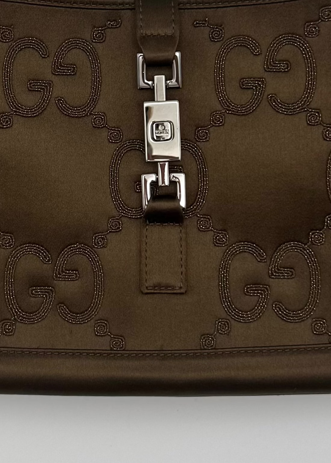 A brown Gucci shoulder bag made of coated canvas with the brand's signature GG monogram pattern and a silver-tone turn-lock closure on the front flap.